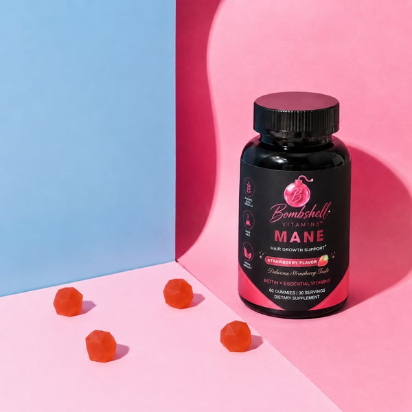 A bottle of Bombshell Mane beside four gummies on a pink and blue background
