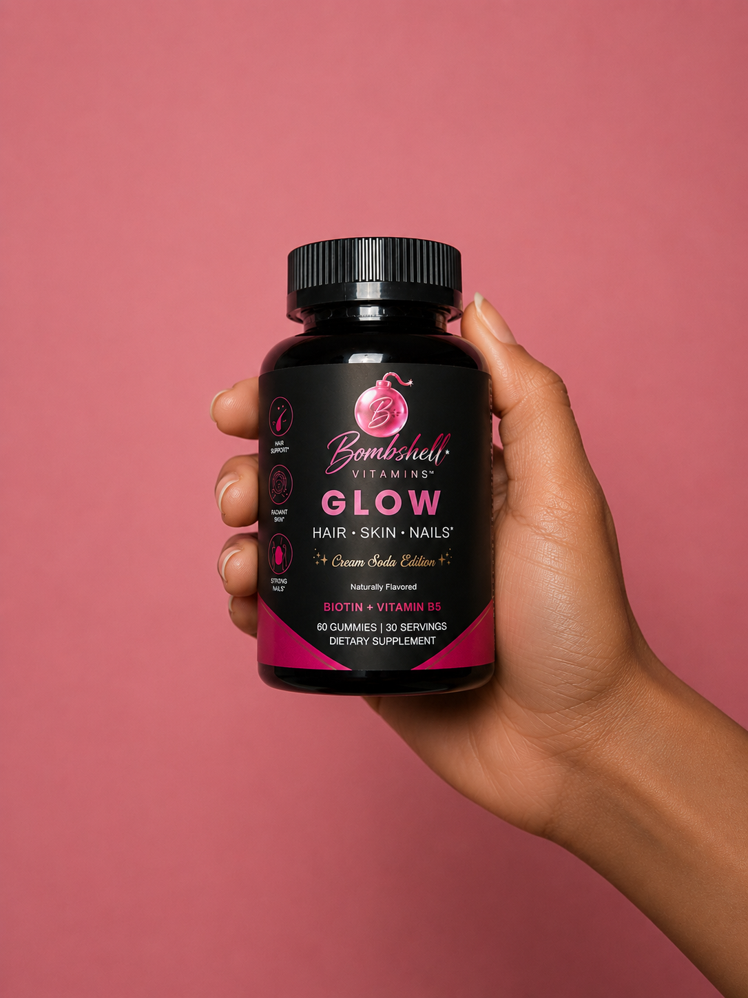 A hand holding a bottle of Bombshell Glow against a pink background